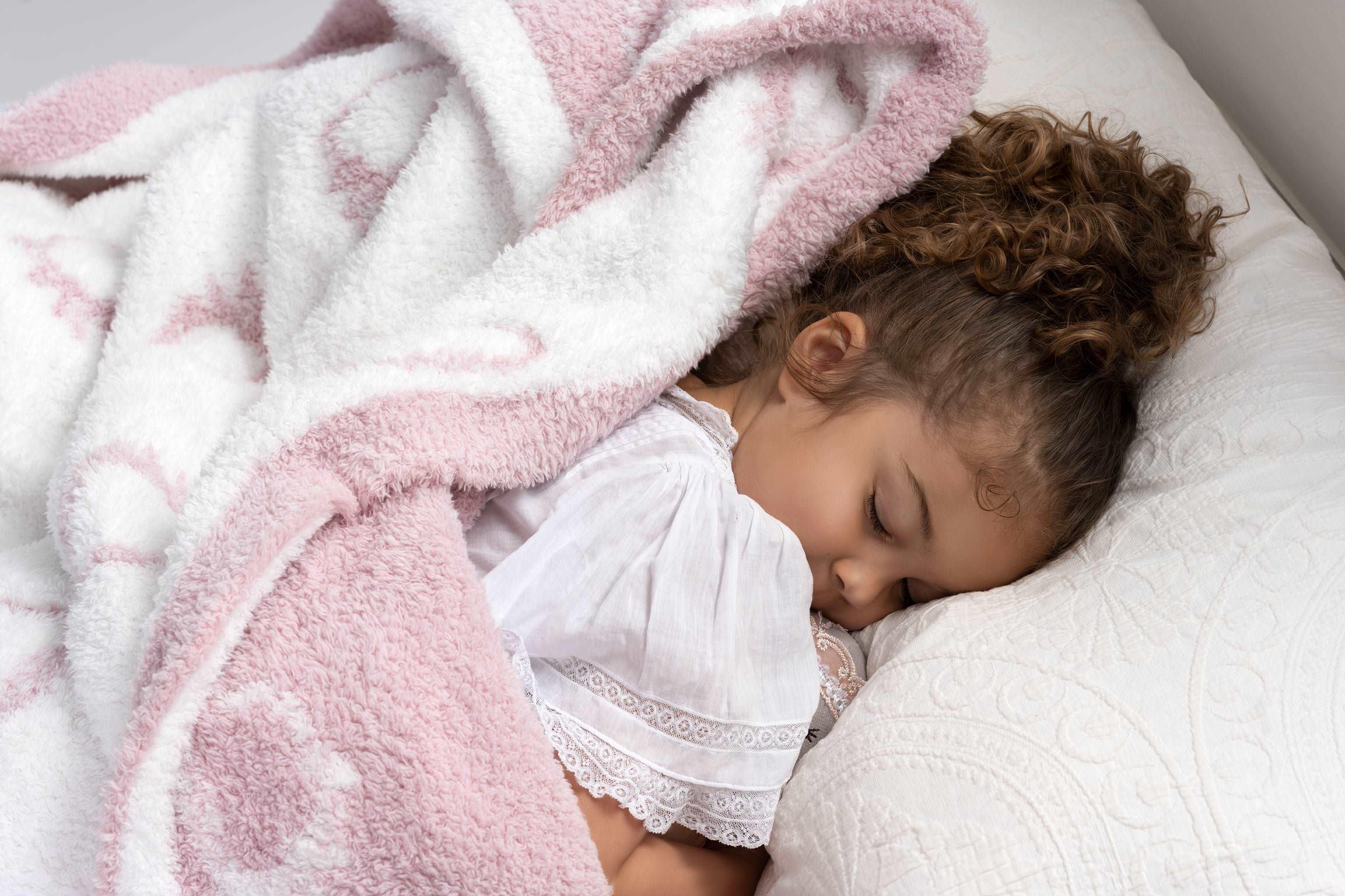 little girl sleeping snuggled up in a plush pink and white throw blanket